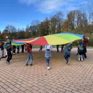 Kinder stehen gemeinsam in einem Kreis und bewegen ein buntes Tuch